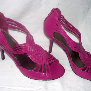 May include: A pair of pink high-heeled sandals with a strappy design. The sandals have a thin heel and a pointed toe.