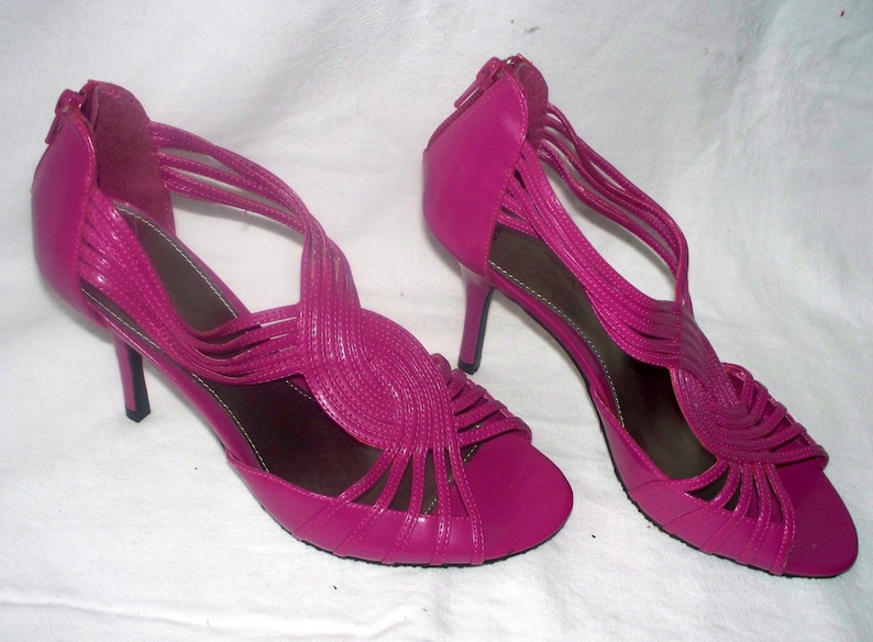 May include: A pair of pink high-heeled sandals with a strappy design. The sandals have a thin heel and a pointed toe.