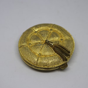 May include: A gold-toned compact mirror with a quilted design and a tassel.