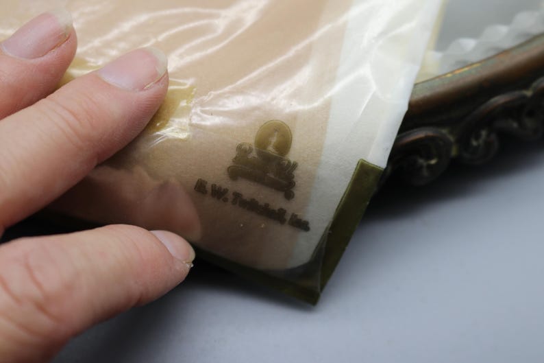 Puede incluir: Primer plano de una bolsa de pl&aacute;stico transparente con un logotipo y texto, sostenida por una mano. El logotipo presenta una imagen estilizada de un edificio y un sol. El texto dice "A.W. Tuthill, Inc."