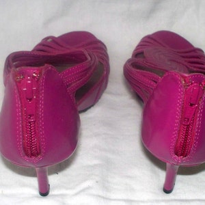 May include: A pair of bright pink high-heeled sandals with a zipper detail on the back. The sandals have a strappy design and are made of a shiny material.