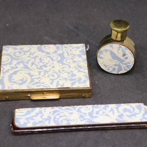 May include: A vintage blue and white vanity set with a compact, a small bottle, and a comb. The set features a delicate floral pattern.