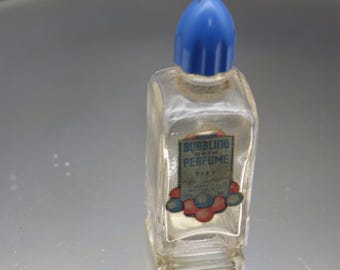 May include: A small, clear glass bottle with a blue plastic stopper. The bottle has a label that reads "Bubbling Bath Perfume" with a red and blue floral design.