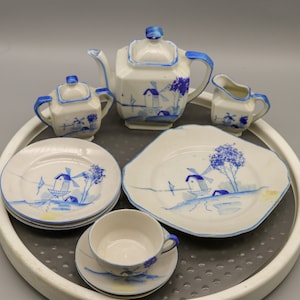 May include: A blue and white porcelain tea set with a windmill design. The set includes a teapot, creamer, sugar bowl, and three saucers with matching plates.