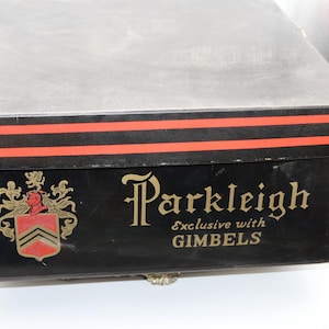 May include: A rectangular black storage box with a lid featuring two horizontal red stripes. The front displays a gold heraldic crest and the gold text Parkleigh Exclusive with GIMBELS. The box has a matte finish and a structured, boxy shape.