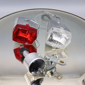 K&ouml;nnte beinhalten: Ein Satz von zwei Vintage-Fahrradlichtern. Das Vorderlicht ist wei&szlig; und das R&uuml;cklicht ist rot. Beide Lichter sind aus Kunststoff und haben eine Chromoberfl&auml;che.