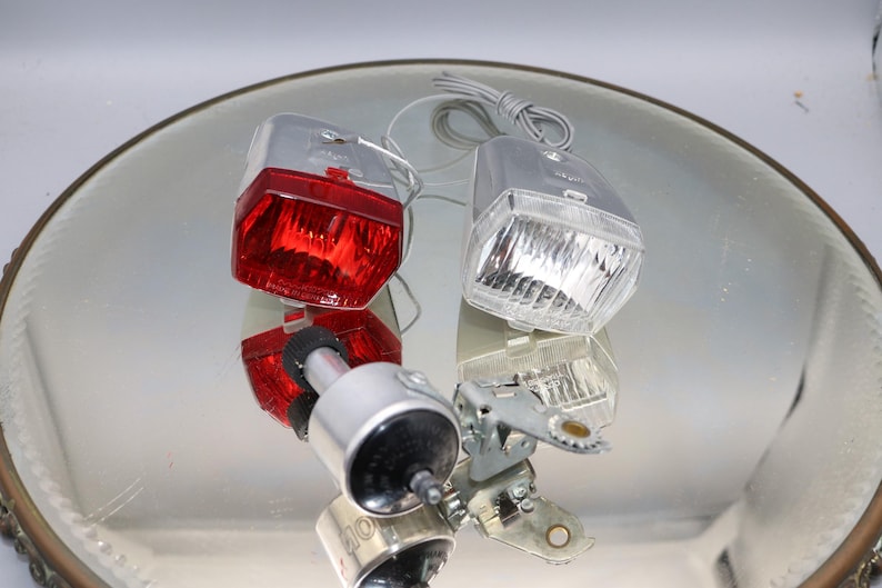 K&ouml;nnte beinhalten: Ein Satz von zwei Vintage-Fahrradlichtern. Das Vorderlicht ist wei&szlig; und das R&uuml;cklicht ist rot. Beide Lichter sind aus Kunststoff und haben eine Chromoberfl&auml;che.