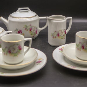 May include: A white porcelain tea set with floral designs. The set includes a teapot, creamer, sugar bowl, two cups, and two saucers.
