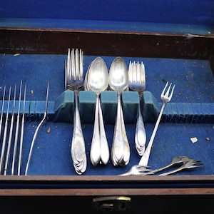 Puede incluir: Una caja de madera con un forro de terciopelo azul que contiene un juego de cubiertos de plata. Los cubiertos incluyen tenedores, cucharas y cuchillos.