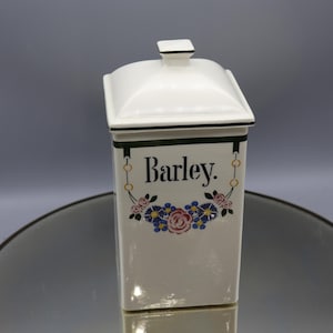 May include: White ceramic canister with a green and gold trim and floral design. The canister has a lid and says "Barley" on the front.