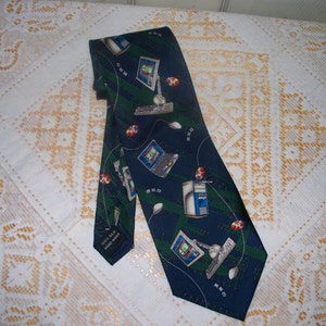 May include: A dark blue silk tie with a repeating pattern of computer monitors, keyboards, and mice. The tie has a white label that reads "100% Silk Hand Made".