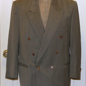 May include: A double-breasted blazer with a striped pattern in a dark gray color. The blazer has four brown buttons and a single button on the cuff.