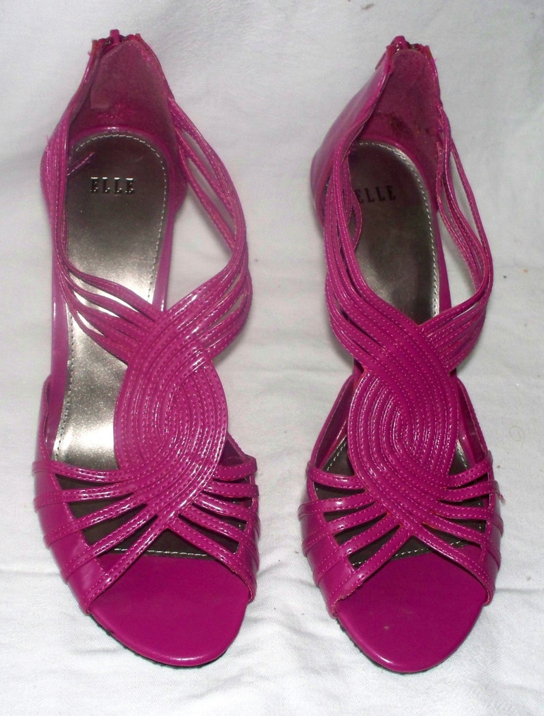 May include: A pair of pink high-heeled sandals with a criss-cross strap design. The sandals have a pointed toe and a back zipper closure. The brand name "ELLE" is visible on the insole.