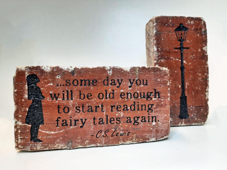 May include: Two rectangular brick art pieces with a rustic appearance. One features a silhouette of a girl and the quote "...some day you will be old enough to start reading fairy tales again." by C.S. Lewis. The other brick has a black silhouette of a street lamp.