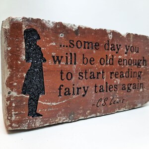 May include: A rectangular brick with the quote "...some day you will be old enough to start reading fairy tales again" by C.S. Lewis. The brick is red-brown with a black silhouette of a girl.