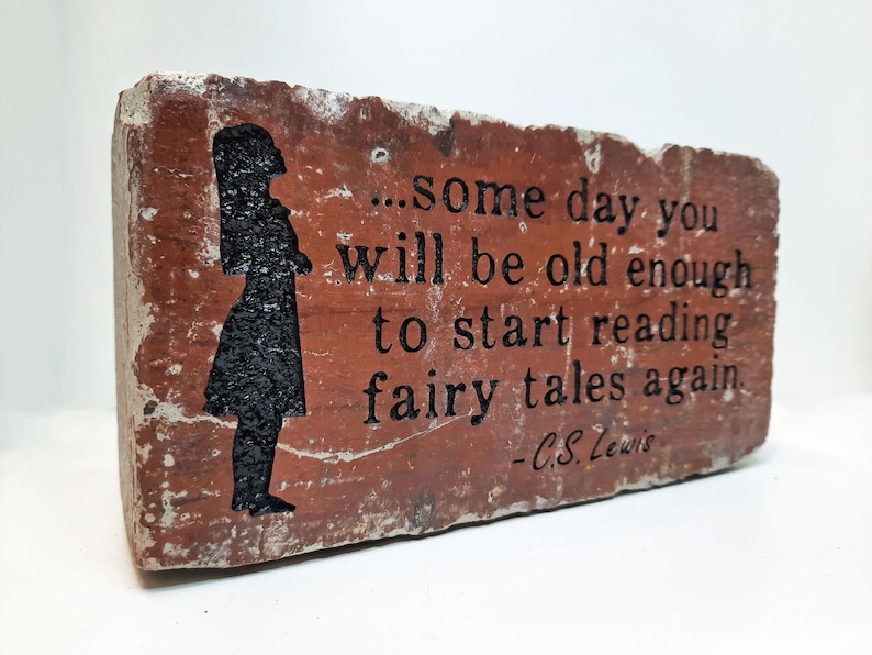 May include: A rectangular brick with the quote "...some day you will be old enough to start reading fairy tales again" by C.S. Lewis. The brick is red-brown with a black silhouette of a girl.