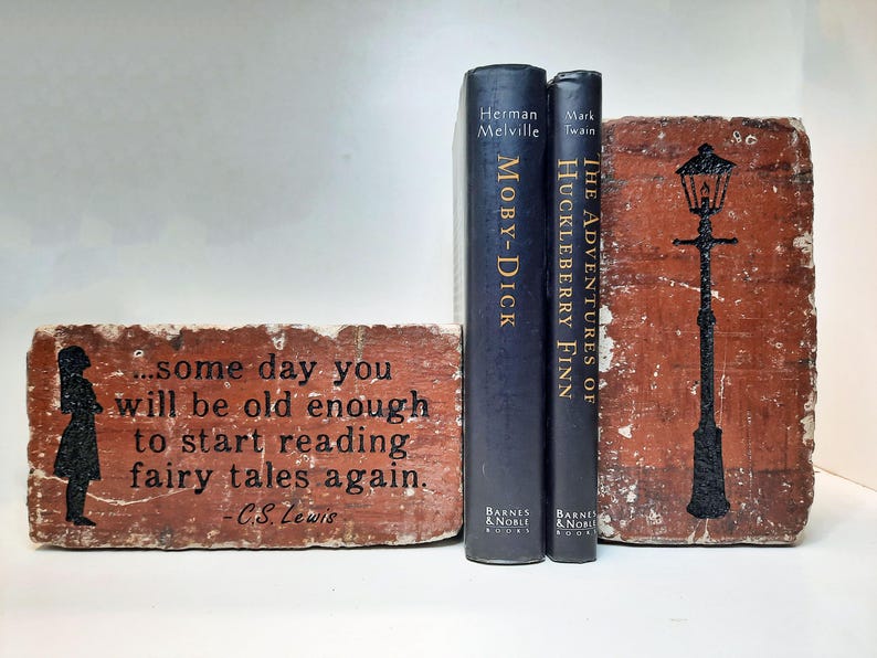 May include: A decorative bookend set featuring two classic novels, "Moby Dick" and "The Adventures of Huckleberry Finn", and two brick-shaped bookends. One bookend has a silhouette of a girl and a quote. The other has a black lamp post design.