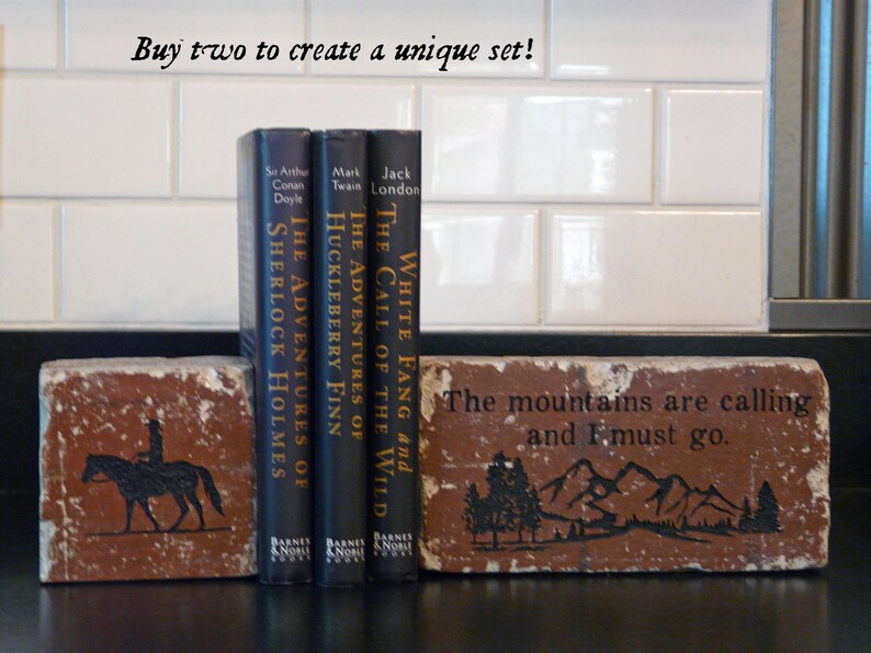 K&ouml;nnte beinhalten: Ziegelstein-Buchst&uuml;tzen mit schwarzen Illustrationen und Text. Eine zeigt einen Reiter auf einem Pferd, die andere eine Berglandschaft mit dem Text "The mountains are calling and I must go." Drei klassische B&uuml;cher stehen dazwischen.