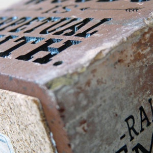 Puede incluir: Primer plano de un ladrillo rectangular y desgastado con las palabras "PERPETUAL YOUTH" talladas en la superficie. El ladrillo es de color marr&oacute;n rojizo con una base de corcho. Tambi&eacute;n es visible el texto "-RALPH ME".
