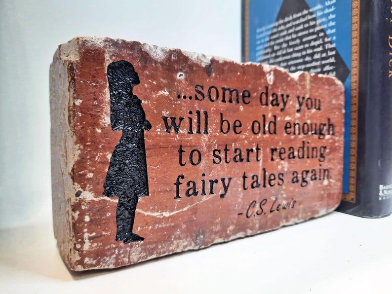 May include: A brick with a quote from C.S. Lewis, "...some day you will be old enough to start reading fairy tales again", alongside a black silhouette. The brick is reddish-brown, with a book in the background.