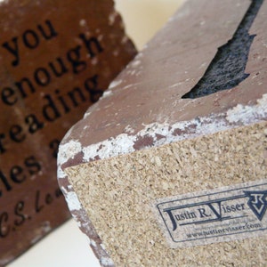 May include: Two rectangular, reddish-brown decorative blocks with white edges. One block features the quote "May you old enough reading short tales - C.S. Lewis" in black text. The other block has a cork base and a "Justin R. Visser" sticker.