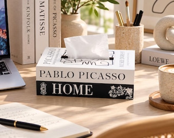 May include: A rectangular tissue box cover designed to look like stacked books. The top section is white with black text reading PABLO PICASSO and MUSEE D'ORSAY. The bottom section is black with the white text HOME and floral accents.