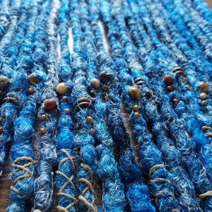 May include: Close-up of blue and white synthetic dreadlocks with brown, white, and orange beads.