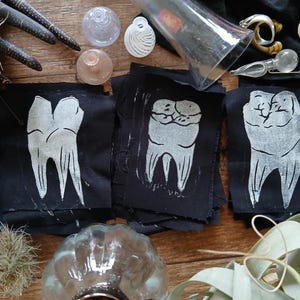 May include: Three black fabric patches with white printed images of teeth. The patches are stitched together and have a rough, textured surface.