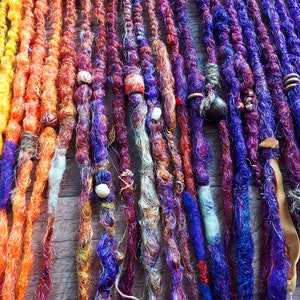 May include: A collection of colorful synthetic dreadlocks with beads and other decorative elements. The dreadlocks are made of a variety of colors, including orange, yellow, purple, and brown.