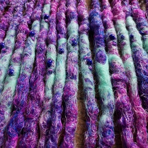 May include: Close-up of a set of synthetic dreadlocks with a mix of purple, pink, and blue colors. The dreadlocks are decorated with small blue beads.
