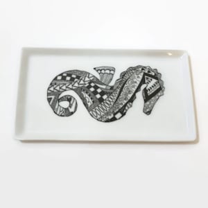 Könnte beinhalten: Ein rechteckiges weißes Keramiktablett mit einem schwarzen und weißen gemusterten Seepferdchen-Design.