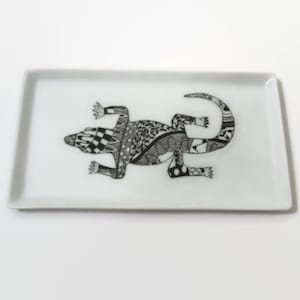 Könnte beinhalten: Ein rechteckiges, weißes Keramiktablett mit einem schwarzen und weißen Muster eines Leguan.