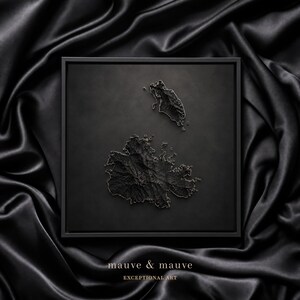 May include: A square black framed wall art piece featuring a three-dimensional topographic map of Antigua and Barbuda in matte black. The text "mauve & mauve" and "EXCEPTIONAL ART" is printed in gold at the bottom of the frame.