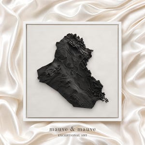May include: A square framed wall art piece featuring a black, three-dimensional topographical relief map of Iraq centred on a light cream background. The text "mauve & mauve" and "EXCEPTIONAL ART" is printed in small black letters below the frame.