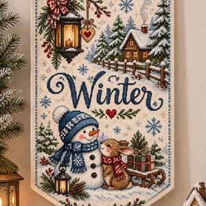 May include: A rectangular cross-stitch wall hanging featuring the word Winter in blue script. The design includes a snowman with a blue hat and scarf, a brown rabbit, a snow-covered cabin, a lantern, and snowflakes on a cream fabric.