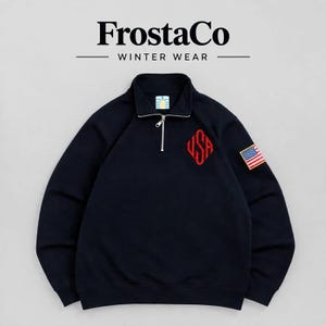 Op de afbeelding: Een marineblauw sweatshirt met een korte rits en de tekst FrostaCo WINTER WEAR bovenaan. Op de borst staat een rood geborduurd USA-monogram in een ruitvorm en op de linkermouw zit een kleine, rechthoekige Amerikaanse vlagpatch.