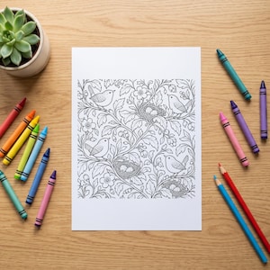 Puede incluir: Una hoja de papel rectangular blanca con una detallada ilustraci&oacute;n de l&iacute;neas en blanco y negro de p&aacute;jaros, nidos con huevos, flores y ramas frondosas, rodeada por un surtido de crayones de cera de colores sobre una superficie de madera clara.