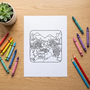 May include: A white sheet of paper featuring a black and white line art illustration of a village scene with two rabbits, wooden houses, a bridge, and mountains, surrounded by a collection of colorful wax crayons on a light wood surface.