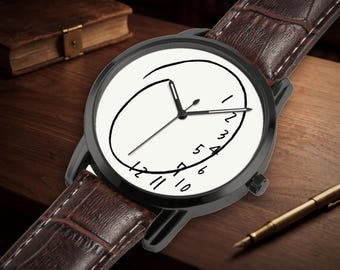 Puede incluir: Un reloj de pulsera con caja circular negra y correa de cuero marrón texturizado. La esfera blanca presenta un contorno circular negro dibujado a mano y números negros del 1 al 12 dispuestos en una secuencia curva no tradicional.