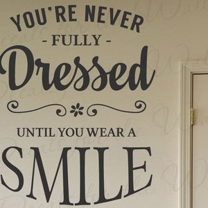 Puede incluir: Pegatina de pared en blanco y negro con el texto "You're never fully dressed until you wear a smile".