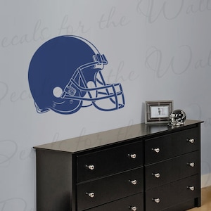 May include: A blue football helmet wall decal on a light blue wall above a black dresser with six drawers.