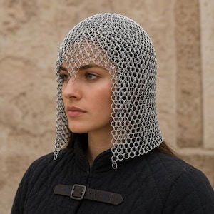 May include: A silver-colored chainmail coif constructed from interlocking metal rings that cover the head and neck. The coif features a scalloped edge along the forehead and hangs down to the shoulders, worn over a black quilted garment.