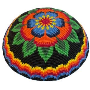 May include: A round, crocheted kippah featuring a black background with a vibrant, multi-colored floral pattern in the center. The design includes shades of blue, orange, red, green, and yellow, with a rainbow-colored border along the edge.