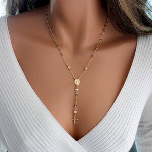 May include: A gold chain necklace with a small cross pendant and a charm of the Virgin Mary. The chain is made of small, gray beads and white pearls.