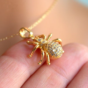 May include: A gold necklace with a sparkling spider pendant. The spider is covered in clear rhinestones.