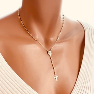 May include: A gold chain necklace with a small pendant featuring the Virgin Mary and a cross. The necklace is on a mannequin wearing a white sweater.