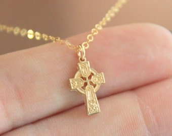 May include: A gold Celtic cross pendant necklace. The cross is detailed with intricate knotwork and is suspended from a delicate gold chain.