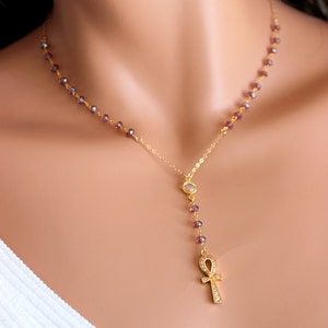 May include: A gold chain necklace with a small clear crystal and an ankh pendant with clear crystals. The necklace is made with small purple beads.