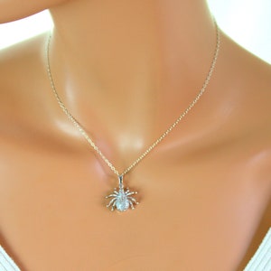 May include: A silver chain necklace with a small, sparkling spider pendant. The spider is made of silver and has clear crystals for eyes.