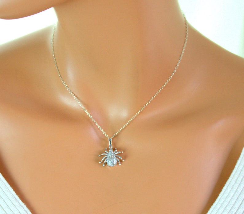 May include: A silver chain necklace with a small, sparkling spider pendant. The spider is made of silver and has clear crystals for eyes.